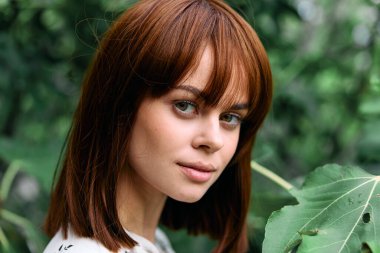 Doğadaki yemyeşil yaprakların arasında poz veren çarpıcı kızıl saçlı.