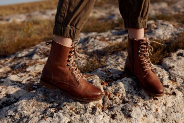 Kahverengi çizmeler tarlanın ortasında duruyor. Arka planda çimenler ve ağaçlar, doğa yolculuğu moda kavramı.