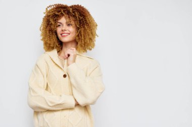 Güzel kıvırcık saçlı neşeli bir genç kadın yumuşak krem renkli bir kazak giyiyor hafif, minimalist arka plan onun ışıl ışıl gülümsemesini arttırıyor, rahatlık ve pozitiflik temalarını vurguluyor.