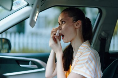 Kadın arabada makyaj yapıyor, dış görünüşüne odaklanıyor, kişisel bakımını sergiliyor, iç mekanı aydınlatan doğal ışık ile sahne günlük hayatı ve özsaygıyı yansıtıyor,