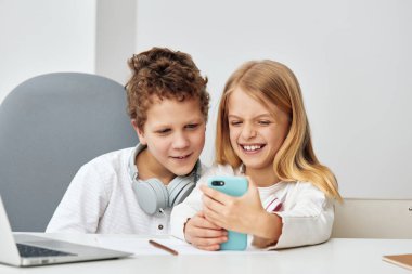 İnternette birlikte ders çalışan mutlu çocuklar, rahat oturma odalarında bir masada oturan bir kız ve bir erkek. Kulaklık takıyorlar, ikisi de bilgisayarlarına doluşmuş ve para kazanıyorlar.
