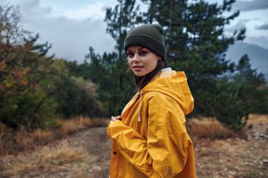 Sarı yağmurluklu genç bir kadın fırtınalı gökyüzü altında toprak bir yolun ortasında duruyor Kırsal kesimde macera yağmurlu bir günde moda gezisi güzelliği vuruyor