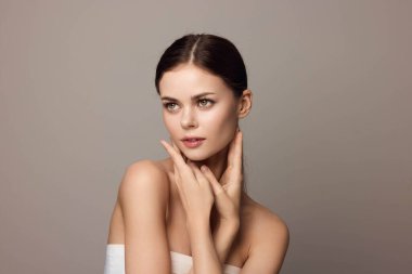 Elleri yüzünde gri arka planda poz veren çekici genç bir kadın. Güzel bir kadın modelin portresi..