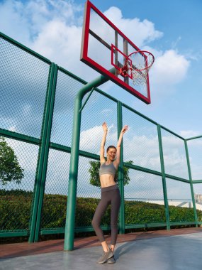 Neşeli sporcu, yeşilliklerle çevrili bir basketbol sahasında kollarını kaldırıyor.