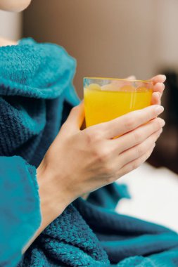 Mavi bornozlu kadın otel odasında, elinde bir bardak portakal suyu ile oturuyor..