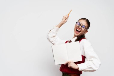 Gözlüklü ve şık giyinmiş neşeli bir kadın, bir elinde boş bir kitap tutarken diğer elinde bir kalemle onun neşeli beyaz geçmişini vurgulayan minimalist beyaz bir arka plana sahip.