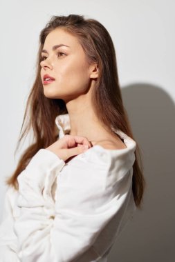 Uzun saçlı ve beyaz bluzlu güzel bir kadının profil portresi, sade beyaz bir arkaplan üzerine kurulmuştur. Kompozisyon onun zarif davranışını ve sakinliğini vurgular.