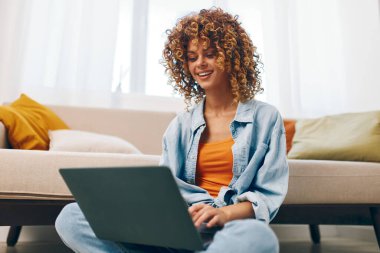 Evde dizüstü bilgisayarda çalışan mutlu bir kadın, rahat oturma odasında online serbest çalışmanın keyfini çıkarıyor.