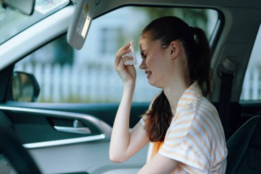 Genç bir kadın, bir arabanın şoför koltuğunda oturur, bir mendille gözyaşlarını silerken görünür bir şekilde üzülür bulanık arka plan ve nazik ışık yalnızlık ve yansıma hissi uyandırır.