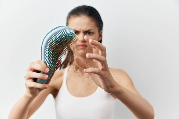 Молодая женщина явно расстроена, когда держит расческу, наполненную волосами в руке. У нее болезненное выражение лица, подчеркивающее эмоциональное воздействие выпадения волос.