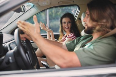 Bir adam ve bir kadın arabadalar, anlaşmazlık duygularını gösteriyorlar. İçerisi parlak ve modern.