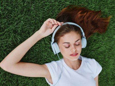 Yazın yeşil çimenlerde kulaklık takmış, gözleri kapalı müzik dinleyen, meditasyon yapan bir kadın. Yüksek kalite fotoğraf