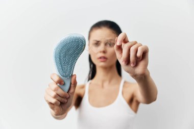 Elinde saç teli olan bir kadın, saç kaybını vurguluyor. Endişeli görünüyor. Arka plan minimalist ve hafif, kişisel bakım ve sağlık bilincini ön plana çıkarıyor.