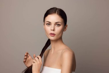 Beyaz elbiseli, gri arka planda poz veren uzun saçlı çekici bir kadın. Zarif bir genç kadının moda fotoğrafı..