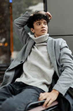 Gri kazaklı ve siyah pantolonlu modacı binanın önünde elleri kafasında oturuyor..