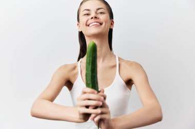 Neşeli genç bir kadın, sağlıklı bir yaşam tarzı ve taze sebzelerin dengeli beslenmedeki önemini gösteren bir salatalıkla poz verir.