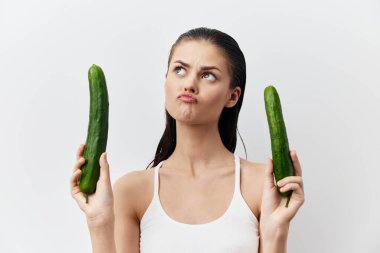 Bir kadın her iki elinde de salatalık tutar, şaşkın bir yüz ifadesi sergiler. Hafif zemin onun düşünceli duruşunu vurgular, sağlıklı beslenmeye ve seçimlere açık yürekliliği somutlaştırır.