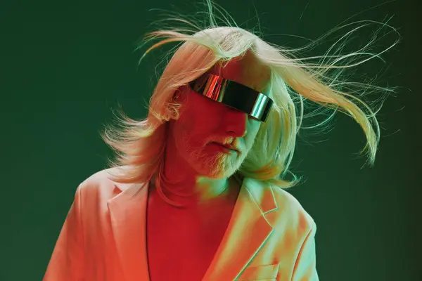 stock image Portrait of a fashionable man with long hair, wearing futuristic eyewear and a white blazer, illuminated by striking green and red lighting, creating a bold and modern aesthetic