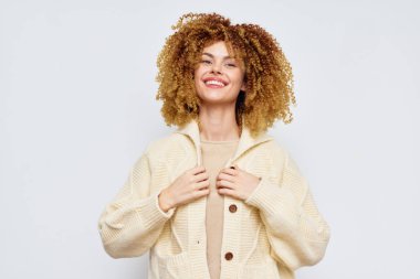 Yumuşak bir süveter giymiş mutlu, kıvırcık saçlı genç bir kadın. Gülüşü ve rahat duruşu, konfor, tarz ve sıcaklık temaları, yaşam tarzı için mükemmel.