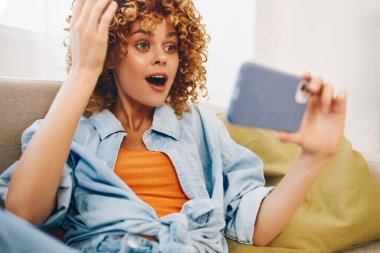 Cep telefonu tutan ve evdeki rahat koltukta dinlenen gülümseyen kadın.