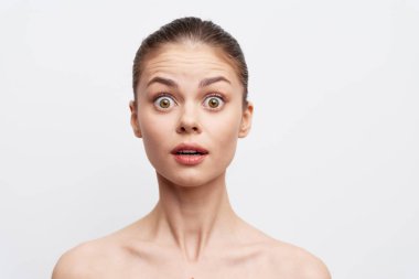 Şaşırmış genç bir kadın, açık bir ağız ve geniş gözler ile minimalist beyaz bir arkaplan karşısında şok ve şaşkınlık dolu bir ifade sergiliyor.