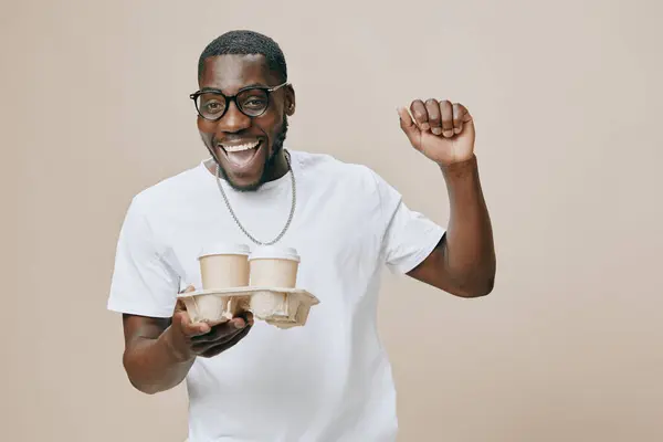 stock image happy male model, wearing casual clothing and glasses, joyfully holding two coffee cups in a neutral colored setting, exuding positive energy with a big smile and an enthusiastic pose, perfect for li