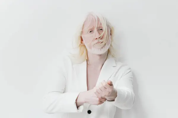 stock image A captivating portrait featuring a pale individual with tousled white hair, dressed in a white blazer The subject stands in a bright, minimalist environment that emphasizes their expressive features