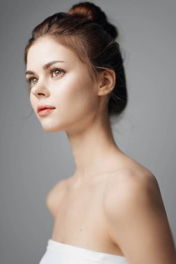 Beyaz elbiseli genç bir kadın gri arka planda bir portrede poz veriyor..