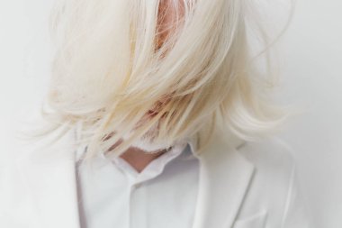 Bu görüntüde yüzünü kaplayan uzun, beyaz saçlı, sanatsal ve duygusal bir hava yayan beyaz takım elbiseli bir kişi var. Konu basit bir arkaplan üzerine kurulmuş.