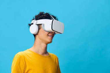 sanal gerçeklik, büyüleyici oyun, renkli arka plan, VR kulaklık ve kulaklık takan genç adam, neşeyle gülümseyen, modern teknoloji, canlı mavi fon, ilgi çekici deneyim