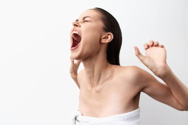 Uzun saçlı bir kadın rahatlatıcı bir ifadeyle esniyor, havluya sarılmış arka plan basit ve minimalistik, duygularını ve sakinliğini vurguluyor.