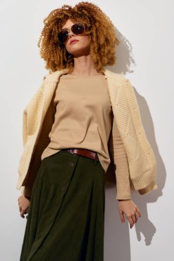 Modaya uygun bir model açık bej bir bluz ve yeşil bir etek giyer, güneş gözlükleriyle aksesuar takar.