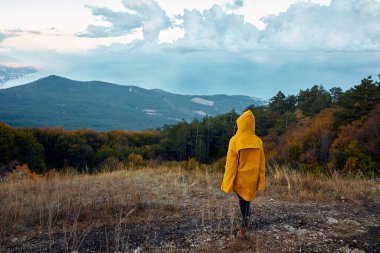 Sarı yağmurluklu bir insanın nefes kesici görüntüsü Tepenin üstünde duruyor Seyahat Macerası Vadisi 'ne bakan