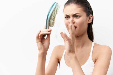 Saç fırçasını beyaz bir arka planda inceleyen, saç durumundan açıkça endişe duyan, hayal kırıklığına uğramış bir kadın, saç bakımı ve güzellik rutinleriyle ilgili duyguları vurguluyor, görebilirlik yaratıyor.