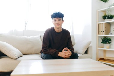 Genç bir adam rahat bir şekilde rahat bir kanepede rahatça oturur, iyi aydınlatılmış, minimalist bir iç mekânda. Sahne, bitkiler ve yumuşak dokularla sükuneti iletir, yaşam tarzı ve modern yaşam kavramları için mükemmeldir.
