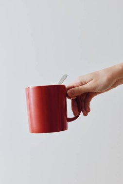 Kırmızı kahve fincanı, beyaz arka planda bir kişi tarafından kaşıkla tutulmuş. metin için kopyalama alanı.