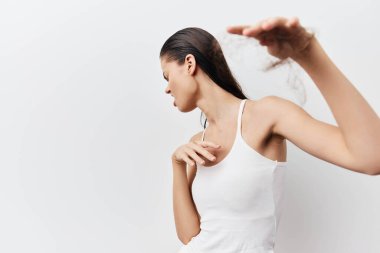 Bir kadın model, zarif bir hareketle, güzelliği ve basitliği ön plana çıkaran, minimalist beyaz bir arkaplana doğru çekilen beyaz bir atlet içinde zarafet ve güven gösteriyor.