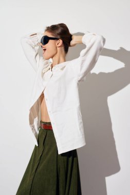 Kendine güveni olan, beyaz bluz ve yeşil etek giyen, temiz beyaz bir arkaplan üzerine kurulmuş modaya uygun bir model.