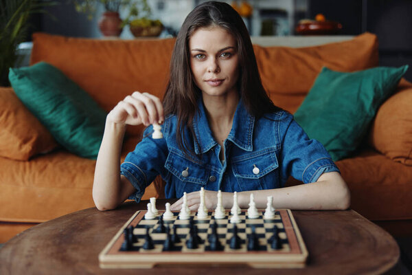 Beautiful young woman enjoying a game of chess in the cozy living room of her home, surrounded by books and plants