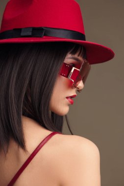 Kırmızı elbise, kırmızı fötr şapka, kırmızı güneş gözlüğü ve gri arka plan tek renkli kırmızı elbiseli şık bir kadın, dikkat çekici kırmızı bir elbise ve fötr şapka, şık kırmızı güneş gözlükleriyle süslenmiş.