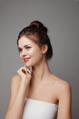 Beyaz elbiseli, eli çenesinde kameraya poz veren, yan yana bakan genç bir kadın. Şık giyinmiş güzel ve zarif bir bayan model. moda fotoğrafçılığı kavramı.