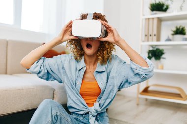 Sanal Gerçeklik Eğlencesi: Mutlu Bir Kadın Evde Fütürist VR Oyunundan Hoşlanıyor, Sanal Gerçeklik Gözlükleriyle Gülümsüyor, Modern Oturma Odasında Bir Koltukta Oturuyor