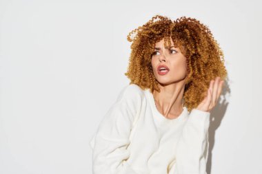 Parlak kıvırcık saçlı, göz alıcı bir genç kadın portresi, temiz beyaz bir zemine kurulmuş, özgüven ve tarz yayıyor, çağdaş güzellik ve moda özünü yakalıyor.