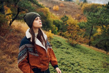 Güzel genç bir kadın, huzurlu bir atmosferi olan renkli ağaçlarla çevrili bir tarlada sonbahar manzarasının tadını çıkarıyor.