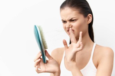 Saçını fırçayla tararken hayal kırıklığına uğramış gibi görünen, saç sağlığı ve güzellik rutinleriyle ilgili konuları vurgulayan, özellikle beyaz bir arkaplan üzerinde duran bir kadının görüntüsü.