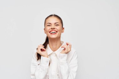 Neşeli bir kadın, ışık saçan tarafsız bir arkaplanda neşeli bir gülümseme, mutluluk ve pozitiflik sergiliyor, neşeli tavırlarını tamamlayan modaya uygun bir kıyafet giyiyor.