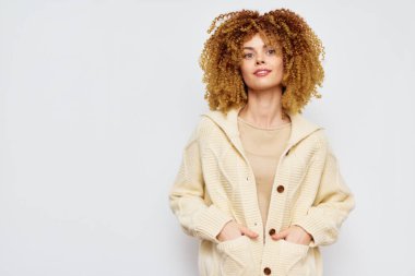 Şehvetli kıvırcık saçlı, rahat bej bir hırka giyen şık bir kadın yumuşak nötr arka plan, hayat tarzı ve moda içeriği için mükemmel olan rahat havayı güçlendirir.