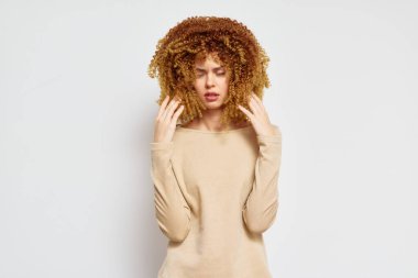 Portrait of a young woman with beautiful curly hair, dressed in a soft beige long sleeve top, set against a clean white background The image reflects emotions of thoughtfulness and serenity clipart