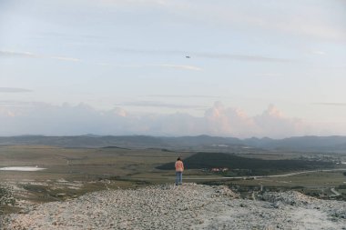 Adventure on top of the world person standing on mountain summit with kite flying in sky clipart