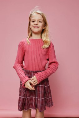 Şık pembe elbiseli ve yüzünde kocaman bir gülümsemeyle, bir stüdyoda güven içinde poz veren genç kız, elinde susuzluğunu simgeleyen bir kitabı tutarken neşe ve heyecan saçar.